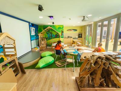 Brightly furnished children's playroom with wooden furniture and cushions in a hotel.