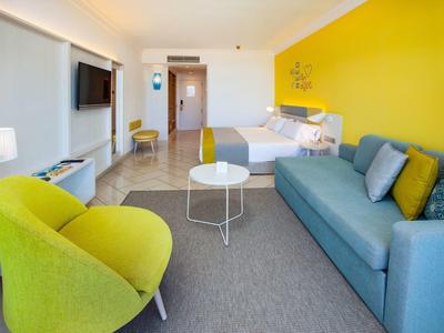 Modern hotel room with yellow wall, green chairs, and blue sofa.