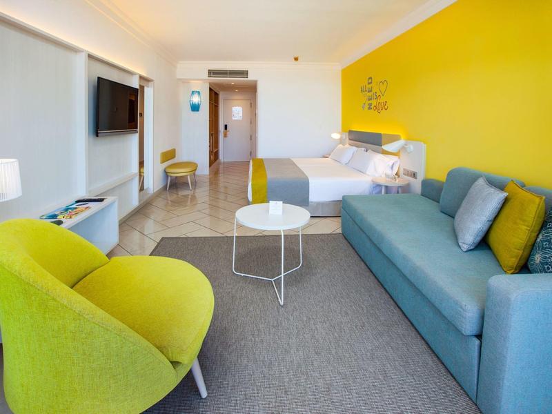 Modern hotel room with yellow wall, green chairs, and blue sofa.