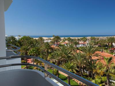 View from a balcony over palm trees towards the sea under a clear blue sky.