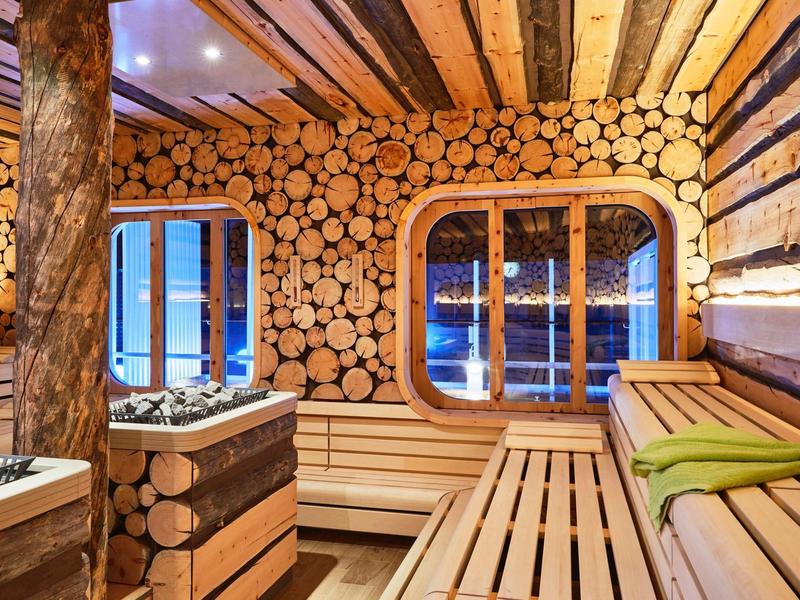 Gezellige houten sauna met bank, handdoeken en wand van houtblokken onder warme verlichting.