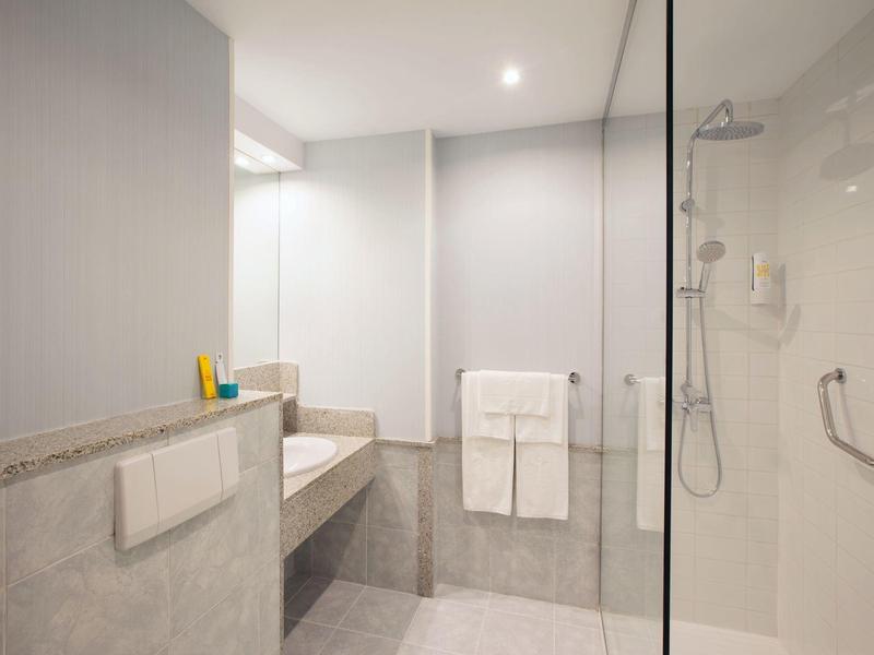 Modern hotel bathroom with walk-in shower, large mirror, and towels on the wall.