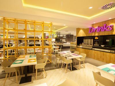 Nowoczesna restauracja z jasnymi stołami, krzesłami i oświetlonym barem z napojami.