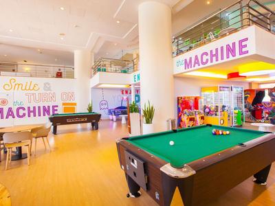 Lichte recreatieruimte met pooltafel, zitplaatsen en spelautomaten in modern design.