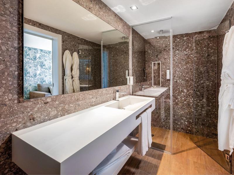 Modern bathroom with marble walls, large mirror, white sink, and glass shower door.