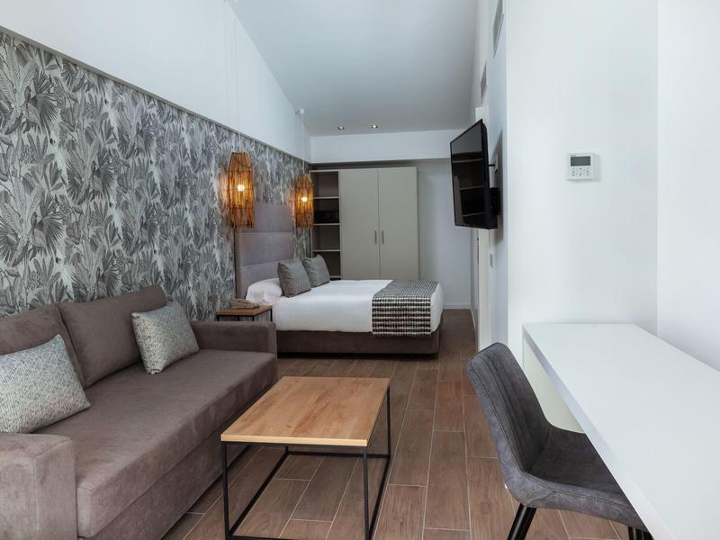 Camera d'hotel moderna con letto grande, divano marrone, scrivania e TV a parete.