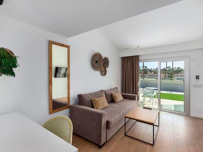 Bright living room with sofa, wooden table, and sliding doors opening to a pool view.