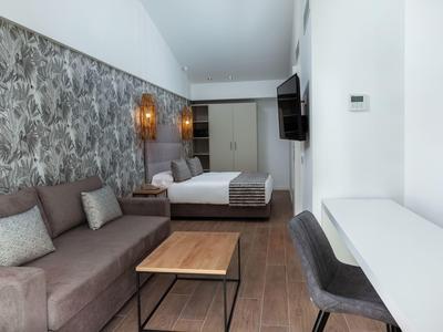 Modern hotel room with a bed, sofa, wooden floor, wall lamp, TV, desk, and chair.
