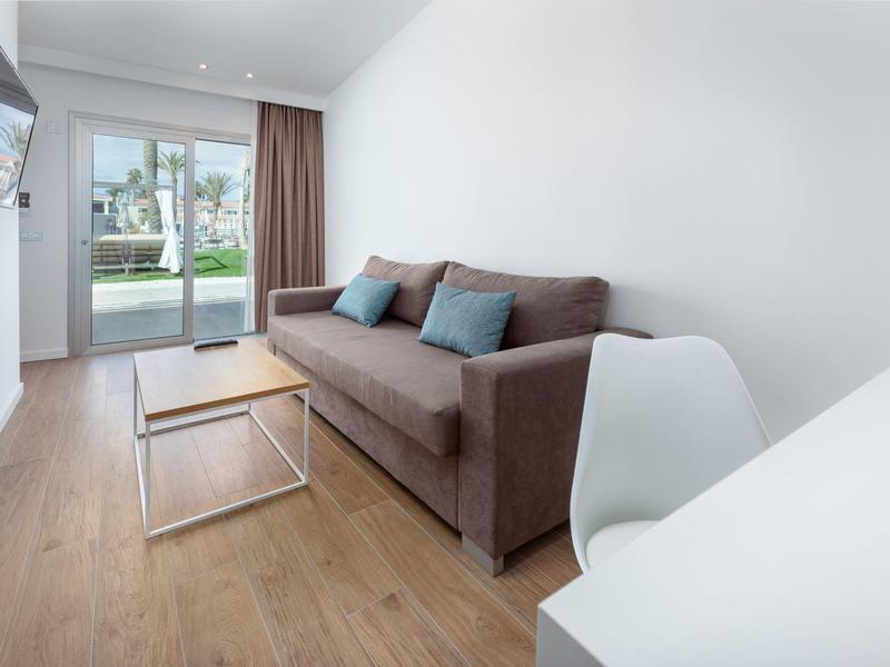 Modern hotel room with sofa, coffee table, TV, and a balcony with a garden view.