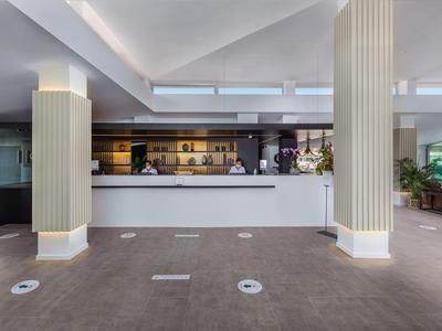 Reception di un hotel moderna con banco bianco, colonne beige e luce naturale.