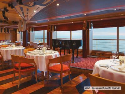 Elegantní restaurace s kulatými stoly, dřevěnými podlahami a výhledem na moře přes velká okna.