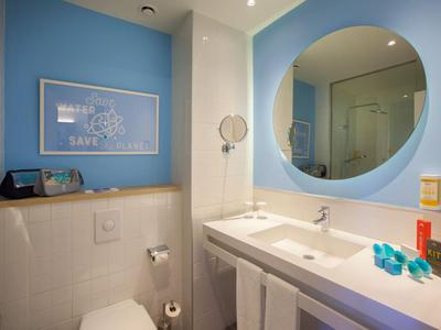Moderne badkamer met wastafel, grote ronde spiegel, toilet en blauwe wanddecoratie.