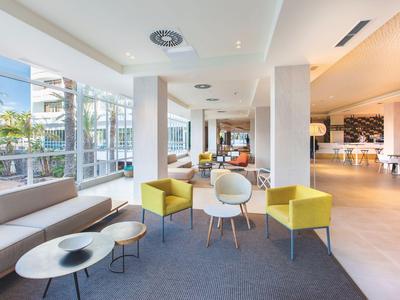 Moderne hotel-loungruimte met banken, fauteuils en grote ramen die daglicht binnenlaten.