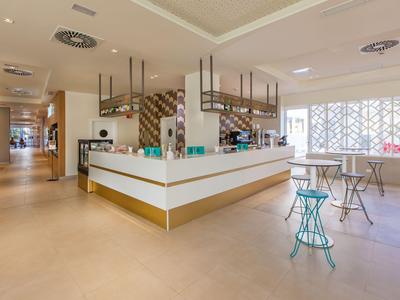 Bar moderno de hotel con colores claros, taburetes y diseño abierto.