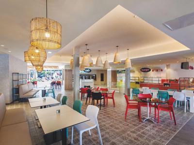 Área de comedor moderna con sillas coloridas y luces elegantes en un restaurante de hotel.