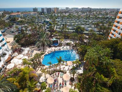 View of an outdoor pool with surrounding loungers and palm trees at a hotel resort near the coast.