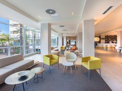 Jasna strefa wypoczynkowa hotelu z nowoczesnymi krzesłami, stolikami kawowymi i dużymi oknami