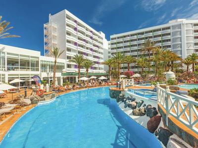 Nowoczesny basen hotelowy z leżakami, palmami i parasolami pod niebieskim niebem.