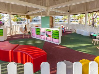 Area giochi per bambini luminosa e colorata con panchine e giochi in uno spazio coperto.