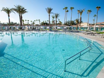 Gran piscina con agua clara y palmeras en un resort soleado.