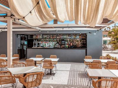 Terrazza di un caffè moderno con sedie in legno, tavoli bianchi e copertura per il sole.