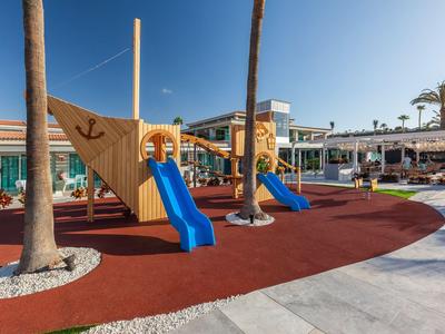 Spielplatz mit Klettergerüst und blauen Rutschen neben Palmen in einer Hotelanlage