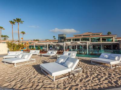 Plage avec des chaises longues blanches devant un hôtel sous un ciel bleu