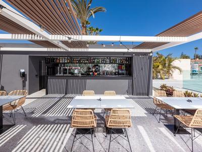Espace bar extérieur moderne avec tables et chaises à côté d'une piscine ensoleillée.