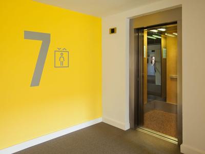 Ascenseur ouvert à côté d'un mur jaune avec grand numéro 7 et symbole de poubelle
