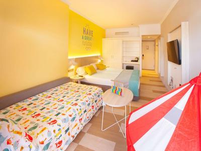 Helles Hotelzimmer mit gelber Wand, zwei Betten und buntem Zelt.