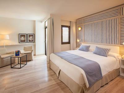 Jasny pokój hotelowy z dużym łóżkiem, strefą wypoczynkową i minimalistycznym wystrojem.