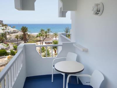Balcon avec rambarde blanche, table et chaises donnant sur des palmiers et la mer.
