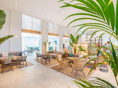 Moderne hotel lounge met planten, banken en tafels in een lichte, uitnodigende ruimte.