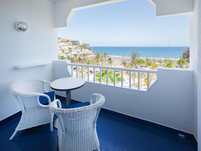 Balkon met twee witte gevlochten stoelen en klein tafeltje met uitzicht op zee.