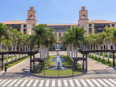Imponente edificio de hotel con fuentes y palmeras en un día soleado.