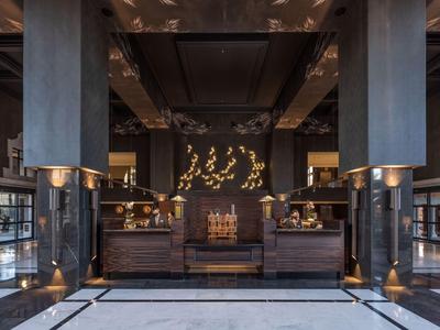 Elegante vestíbulo de hotel con interiores oscuros, decoraciones doradas y mostradores de recepción.