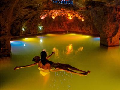 Personne se détendant sur un matelas pneumatique dans une piscine de grotte éclairée à l'eau chaude.