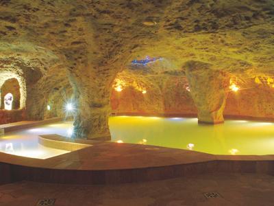 Innenansicht einer unterirdischen, beleuchteten Höhle mit Wasserbecken und Felswänden.