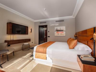 Lichte hotelkamer met tweepersoonsbed, zithoek, tv en moderne inrichting.