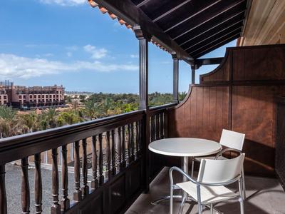 Balkon met tafel en twee stoelen met uitzicht op een hotelcomplex en blauwe lucht.