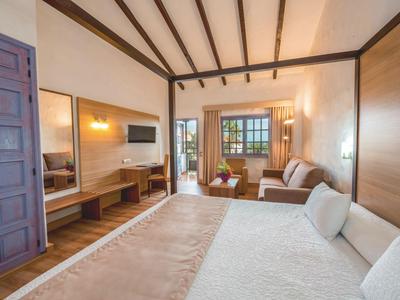 Camera d'hotel luminosa con letto matrimoniale, zona soggiorno, scrivania e finestre con cornici in legno.