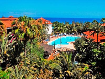 Vista de una piscina de hotel tropical con palmeras y edificios de techo rojo junto al mar