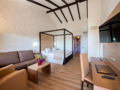 Chambre d'hôtel lumineuse avec lit double, télévision, bureau et coin salon avec canapés.