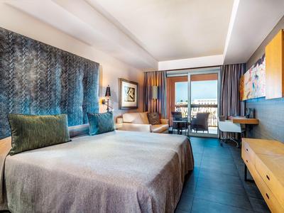 Modernes Hotelzimmer mit großem Bett, Sitzbereich und Balkon mit Blick nach draußen.