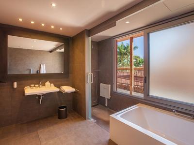 Modernes Badezimmer mit großer Badewanne, Spiegel und Fenster mit Blick auf Palmen.