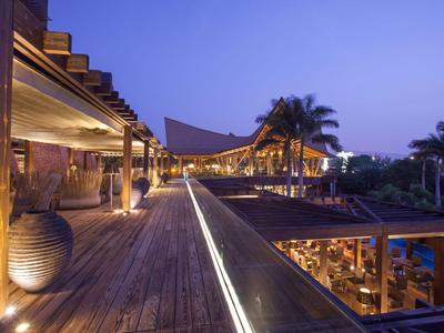Vista nocturna de una elegante plataforma de madera iluminada con entorno tropical y arquitectura moderna.