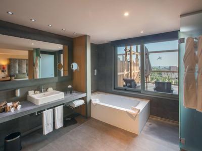 Baño moderno de hotel con bañera independiente, lavabo y ventana grande con vista.