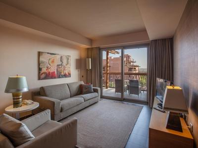 Habitación de hotel moderna con sofá, sillones y balcón con vistas a edificios.