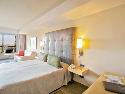 Camera d'hotel luminosa con letto grande, zona salotto e finestra con vista sulla città.