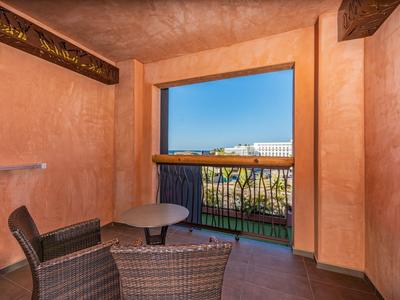 Balkon mit Korbstühlen und Tisch, Blick auf Gebäude unter blauem Himmel.